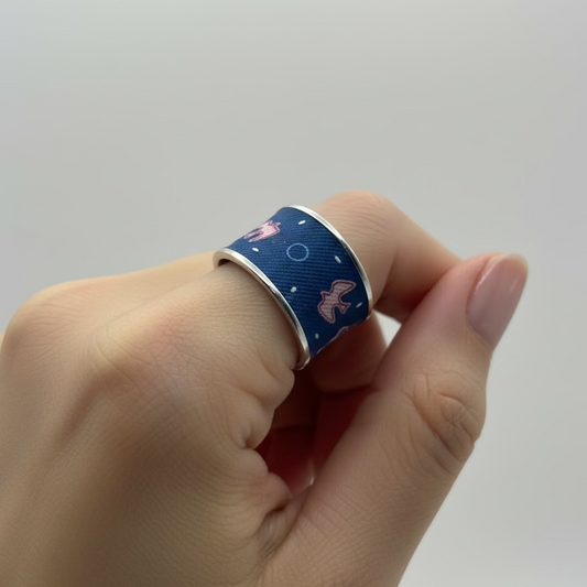 Bague acier et soie bleu marine et rose portée à l'index sur une main de femme.