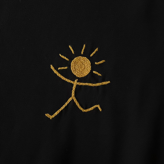 Logo félicita-créations, bonhomme solaire, brodé main en jaune sur un tee-shirt en coton bio noir